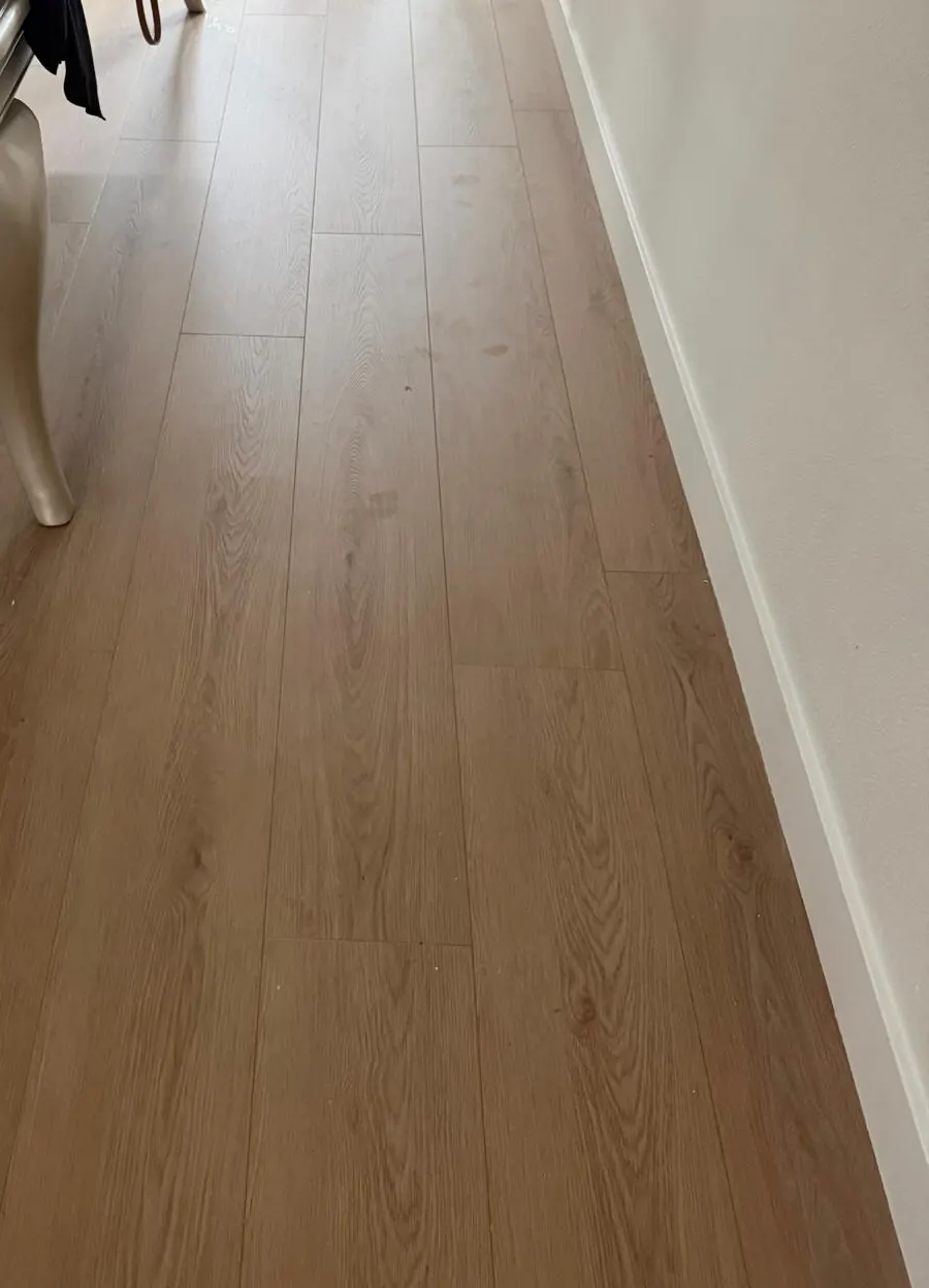 Newly installed plank flooring along a hallway with white baseboards