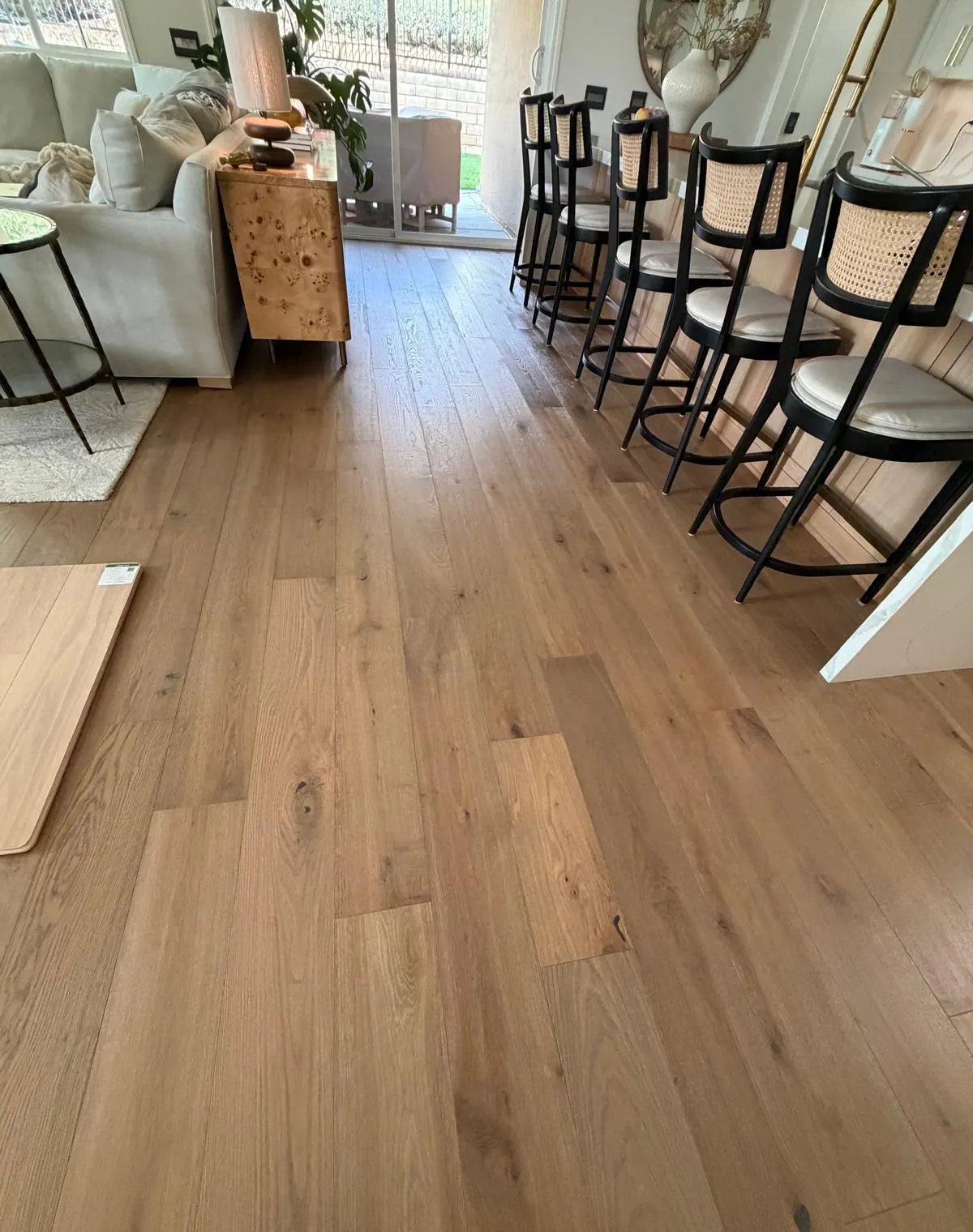 Long run of warm wood-look plank flooring beside a breakfast bar with woven stools