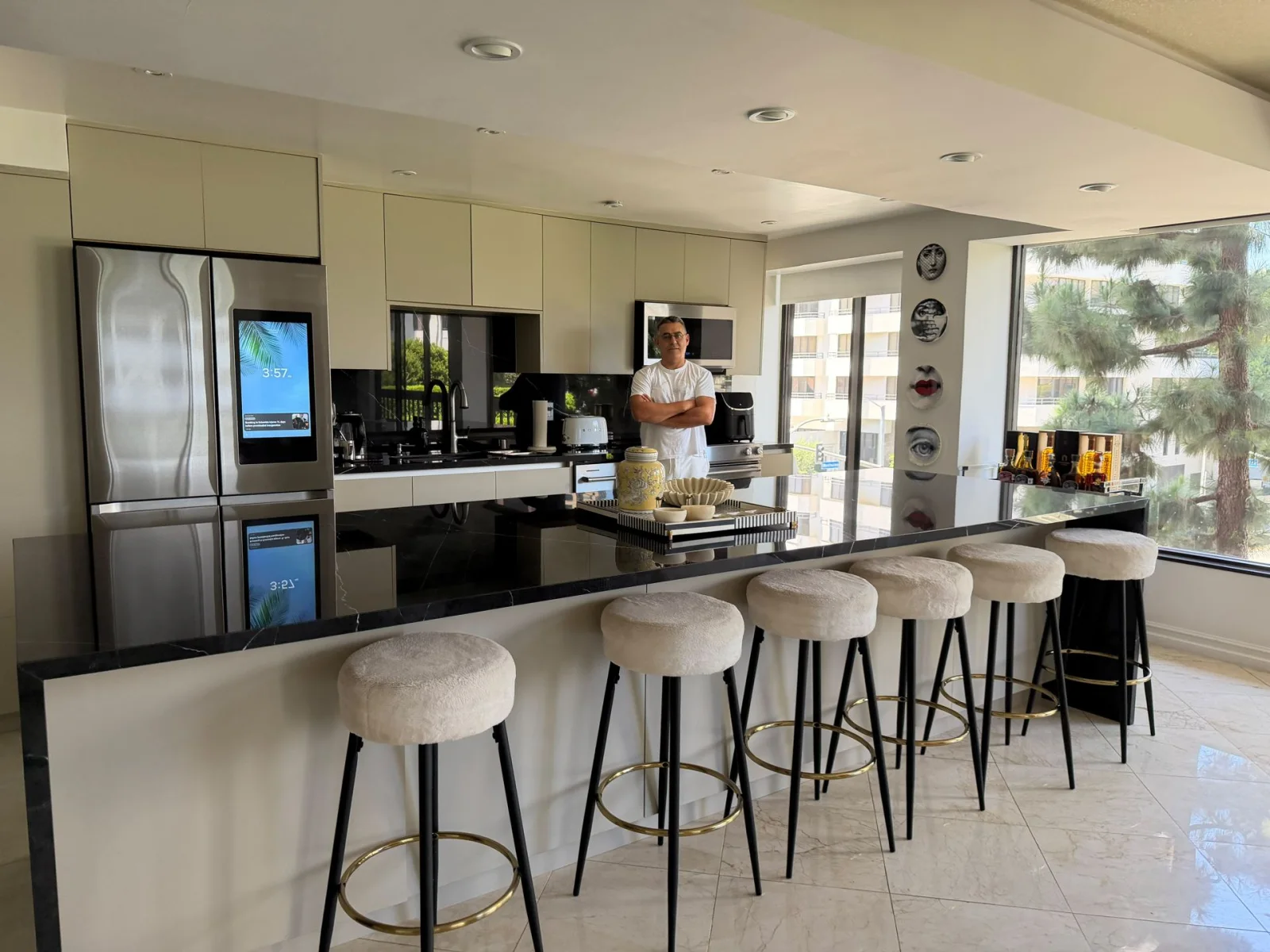 Long kitchen island with white stools, a stainless refrigerator and a pale floor