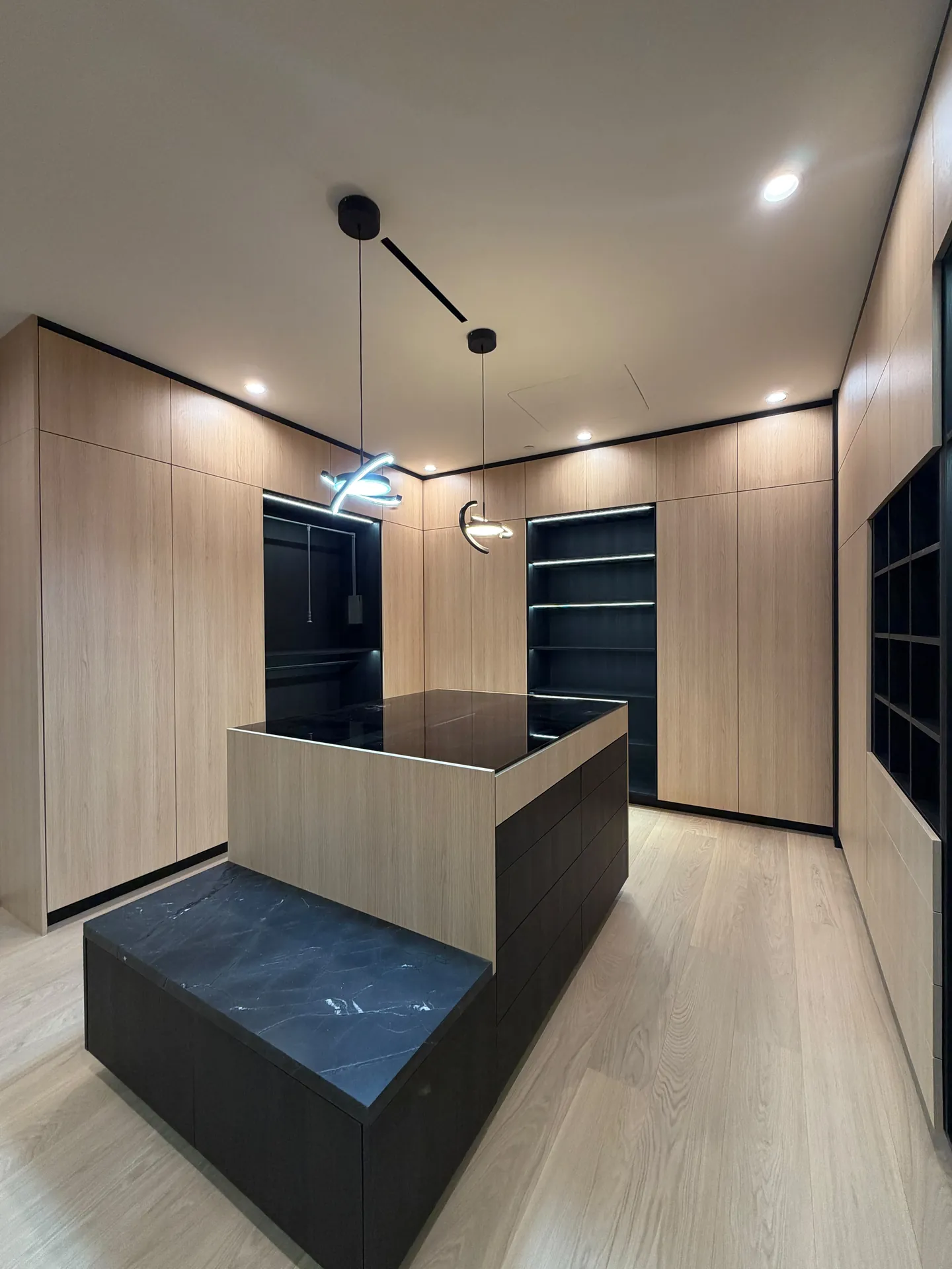 Walk-in closet with wood grain wardrobes, a stone topped center island and pendant lights over a light plank floor