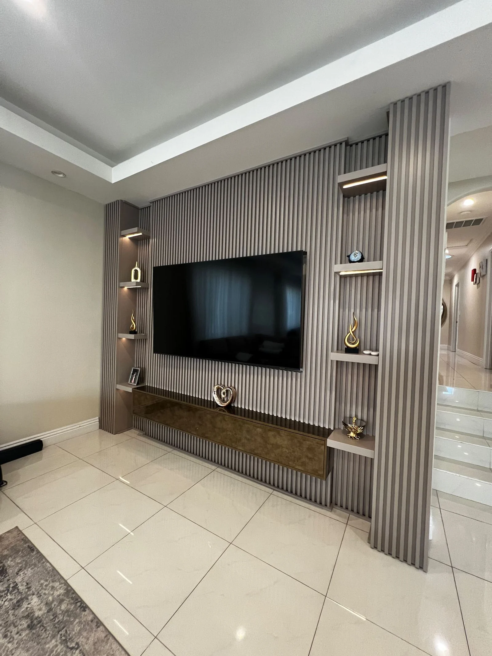 Living room media wall with fluted panels and floating shelves above a glossy white tile floor