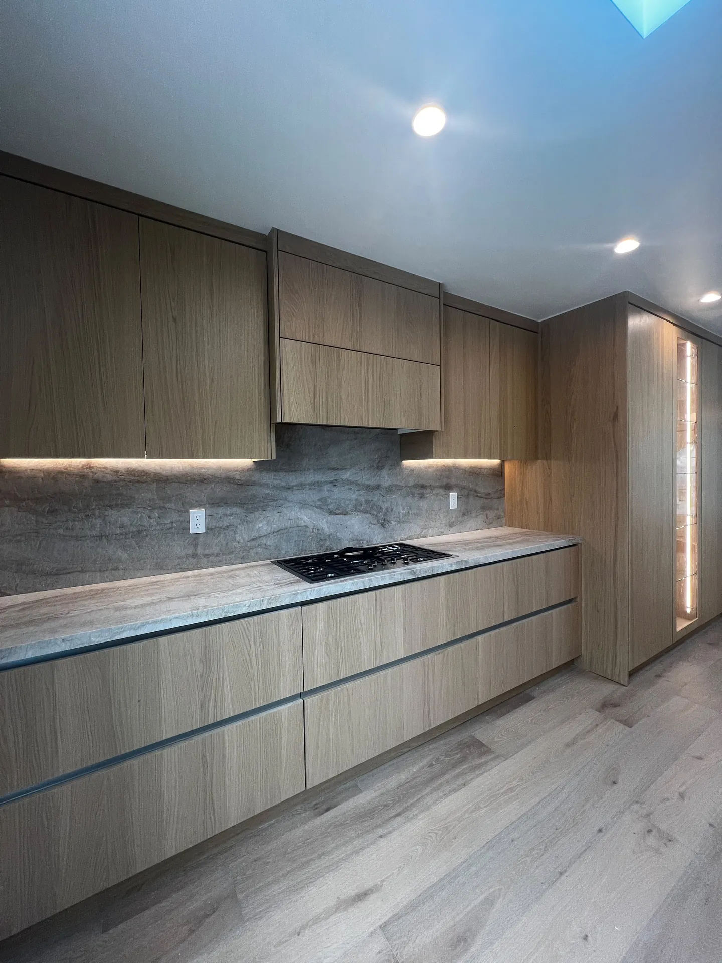 Kitchen with wood grain flat panel cabinets, under cabinet lighting, a stone backsplash and a soft gray plank floor