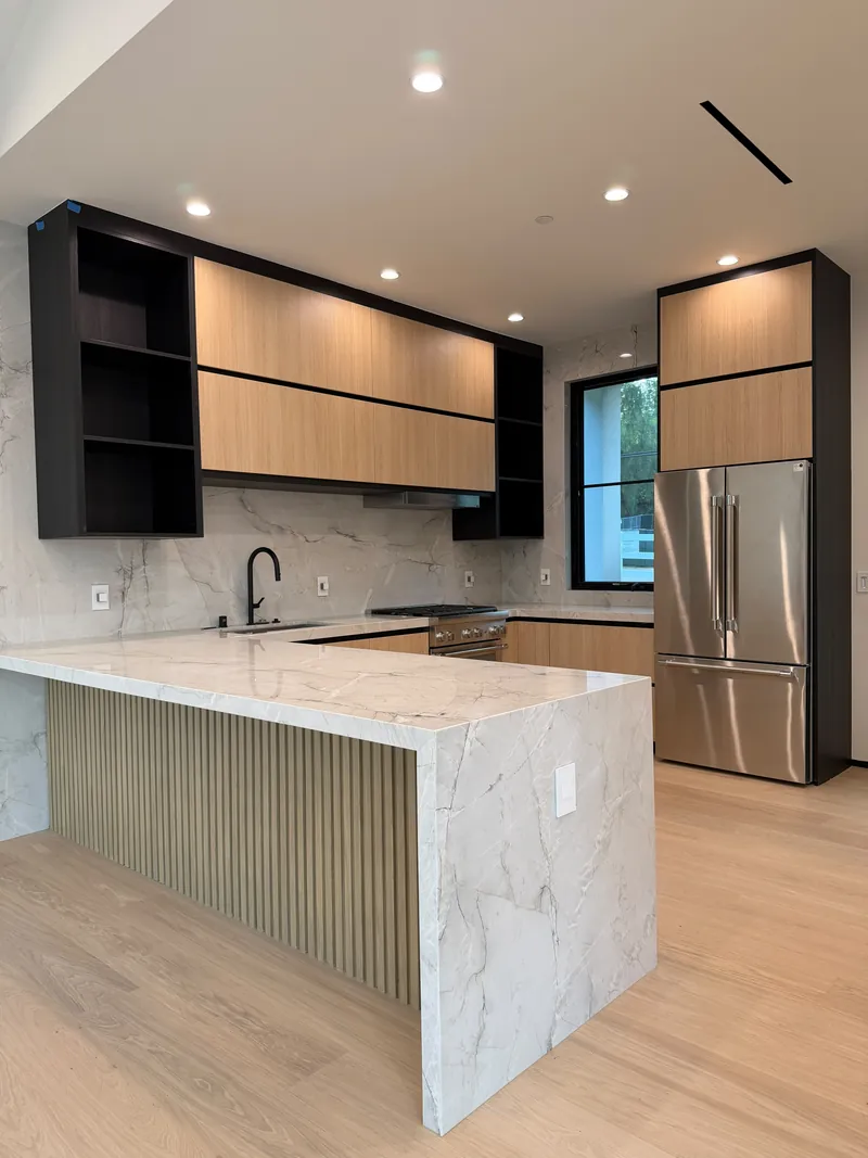 Kitchen with a white marble waterfall peninsula, fluted wood base and light wood floor
