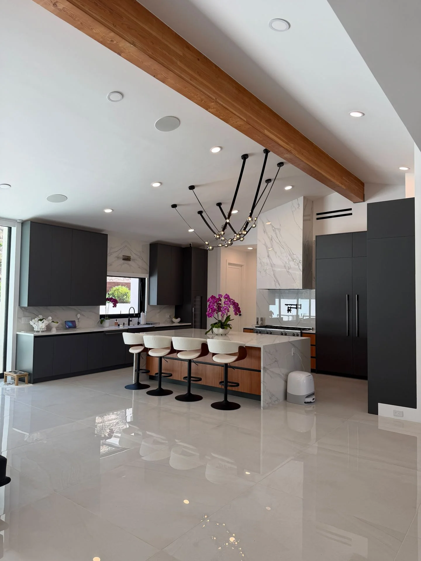 Open kitchen and living area with a wood beam ceiling, black island stools and polished large format floor tile